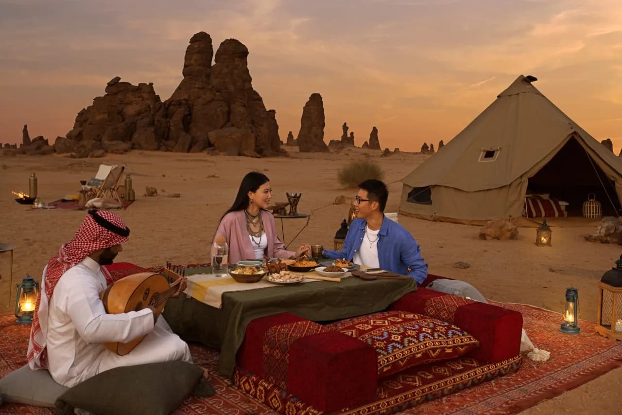 A luxury glamping setup in the AlUla desert with candlelit dining amid sandstone formations at sunset