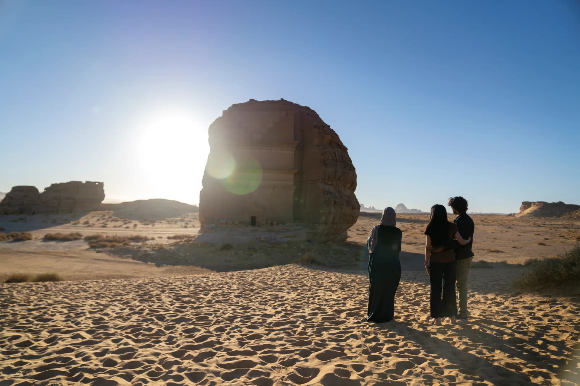 The golden sandstone tomb facades of Hegra glowing in late afternoon light, with the vast AlUla desert stretching behind them
